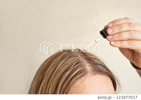 Female applying hair serum with dropper to blonde hair for healthy scalp 123877017