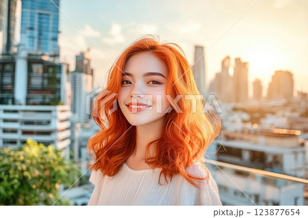 Bright sunset casts a warm glow on a smiling young woman with vibrant red hair in a cityscape 123877654