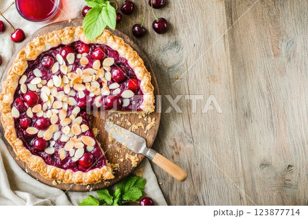Cherry pie with almond topping served on wooden board in a rustic kitchen setting 123877714