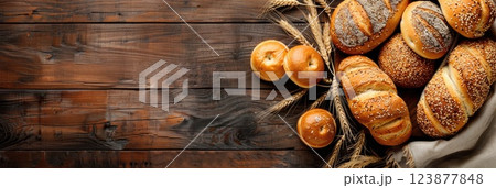 horizontal banner for a bakery, ears of wheat, frame of an assortment of loaves of bread and cereal rolls, brown wooden background, copy space, free space for text 123877848