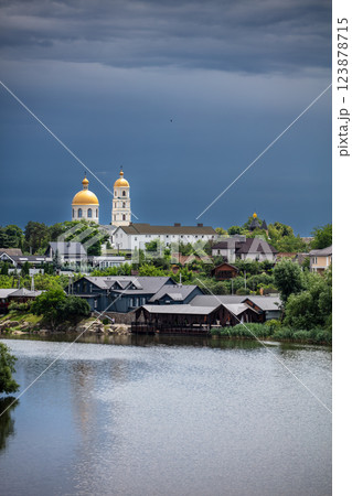 A picturesque town with a river in the foreground, lush greenery, and golden-domed churches in the background. The dramatic sky adds contrast, creating a serene yet moody atmosphere. 123878715