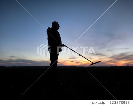 The silhouette of a treasure hunter at sunset. Treasure Hunter - Gold digger - Man Holding Metal Detector 123878938
