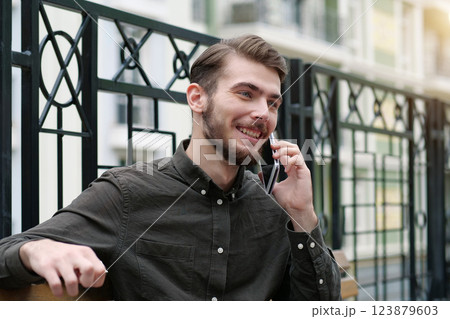 Handsome businessman sits on bench, speaks on cell phone and smiles Handsome businessman sits on bench, speaks on cell phone and smiles 123879603