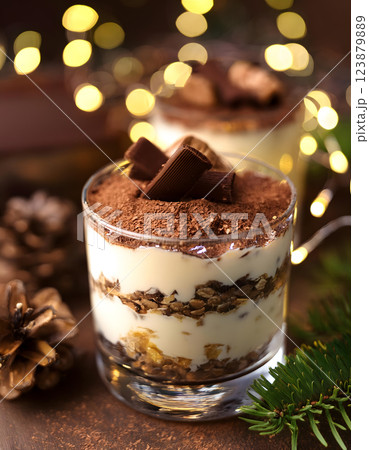 Festive dessert in a glass with layers of cream, chocolate, and crumbs, topped with cocoa powder and a sprig of greenery, surrounded by pinecones and spices Festive dessert in a glass with layers of cream, chocolate, and crumbs, topped with cocoa powder and a sprig of greenery, surrounded by pinecones and spices 123879889