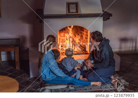 Family bonding by the fireplace during cozy winter evening. Warm and peaceful family moment indoors. Togetherness, love, and relaxation concept. A warm and inviting scene featuring a lit fireplace 123879935