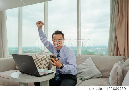 Businessman Joyfully Celebrates Success at Home Office with Laptop in Front Businessman Joyfully Celebrates Success at Home Office with Laptop in Front 123880920