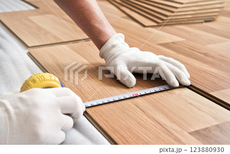 Installing laminated floor, detail on man hands in white gloves holding measuring tape over wooden tile 123880930