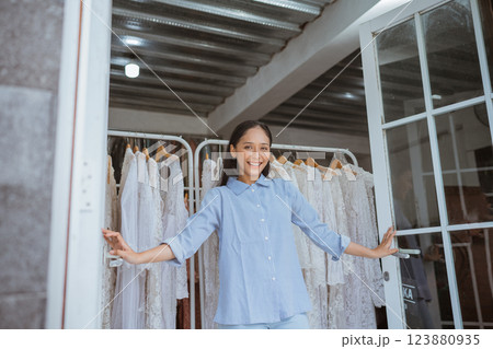 Joyful Girl in Boutique Surrounded by Beautiful and Elegant Dresses Displayed 123880935