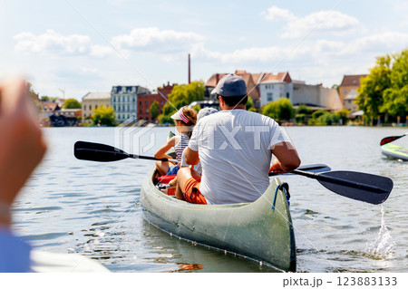 Man with two children enjoy having fun paddling canoe rent across lake river water wearing bright orange life vests hot sunny summer day. Healthy recreational activity lifestyle vacation trip journey 123883133