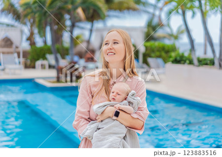 A mother holds her baby near a tropical pool, surrounded by lush greenery. This heartwarming moment captures family bonding, maternal love, and the serene beauty of a tropical getaway, perfect for A mother holds her baby near a tropical pool, surrounded by lush greenery. This heartwarming moment captures family bonding, maternal love, and the serene beauty of a tropical getaway, perfect for 123883516