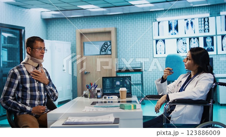 Indian female physician with disability consulting a patient in office, recommending treatment and recovery plan at the hospital. General practitioner meeting with young man. Camera B. 123886009
