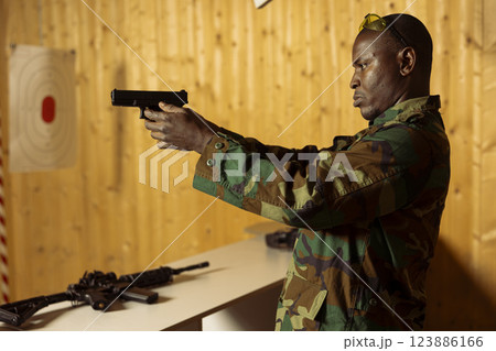 Man in uniform at shooting range doing training designed to increase safety and survivability in combat. African american military unit practicing with pistol to increase handgun handling efficiency 123886166