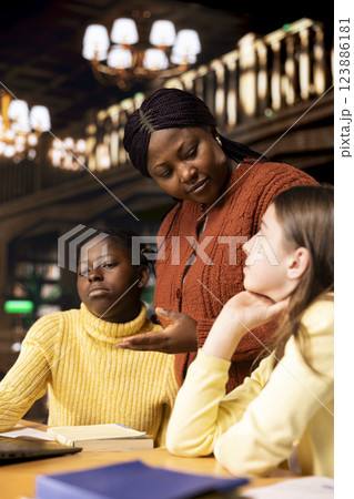 Two preteens girls and their teacher collaborating on schoolwork at the library, focused on academic success and learning development. Students collect extra information with private lessons. 123886181
