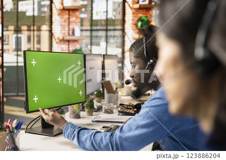 Call center agent at green screen PC answering customers technical inquiries about hardware issue. Customer support employee doing job using chroma key computer to troubleshoot problems 123886204