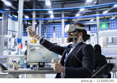 Photovoltaics factory engineer using VR gear to conduct robotic machinery testing. Solar panels plant expert using virtual reality technology to consult manufacturing parameters, making adjustments Photovoltaics factory engineer using VR gear to conduct robotic machinery testing. Solar panels plant expert using virtual reality technology to consult manufacturing parameters, making adjustments 123886240