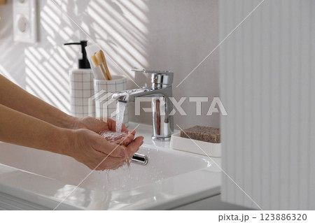 Female hands close up near white clean washbasin with running clean water. Female hands close up near white clean washbasin with running clean water. 123886320