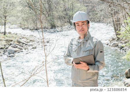 川・河川で河川調査・水質調査をする作業服姿の施工管理技士の男性 123886854
