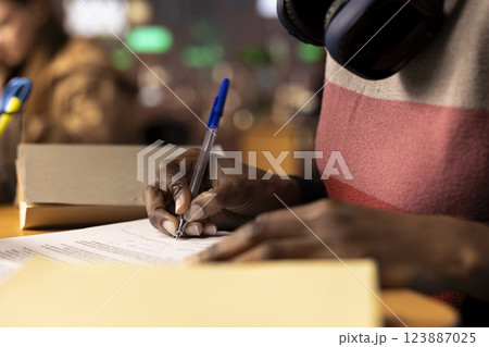 Black university scholar completing a detailed course project using educational resources and materials from the college library general database. Girl working hard on her academic notes. Close up. Black university scholar completing a detailed course project using educational resources and materials from the college library general database. Girl working hard on her academic notes. Close up. 123887025
