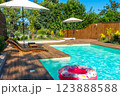 Modern backyard swimming pool with turquoise water, wooden deck, umbrellas, lounge chairs, and pink inflatable float 123888588