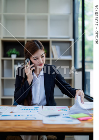 Professional businesswoman engaged in smartphone call by calculator to calculate finance with using stock marketing charts, notebook, and laptop in office Professional businesswoman engaged in smartphone call by calculator to calculate finance with using stock marketing charts, notebook, and laptop in office 123888756