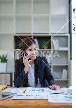 Professional businesswoman engaged in smartphone call by calculator to calculate finance with using stock marketing charts, notebook, and laptop in office Professional businesswoman engaged in smartphone call by calculator to calculate finance with using stock marketing charts, notebook, and laptop in office 123888762