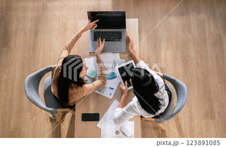 Two women are sitting at a table with laptops and papers in front of them 123891085