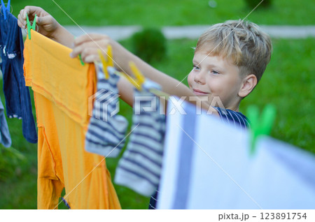 A happy caucasian 9 years boy helps her mother to hang up clothes. Development of fine motor skills through household activities. Selective focus. A happy caucasian 9 years boy helps her mother to hang up clothes. Development of fine motor skills through household activities. Selective focus. 123891754