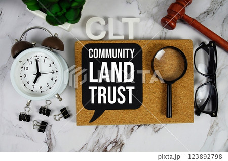 CLT - Community Land Trust acronym with alarm clock and magnifying glass, communication concept background 123892798