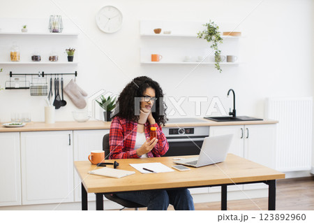 African woman mid 20s conducting online consultation about medication, seated in modern kitchen African woman mid 20s conducting online consultation about medication, seated in modern kitchen 123892960