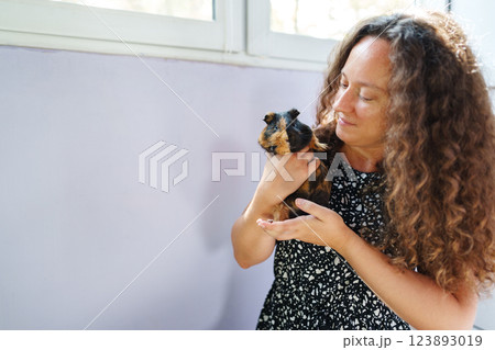 Woman holding a guinea pig in a cozy indoor setting during daylight 123893019