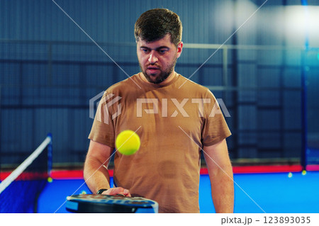 Man practicing tennis skills with a yellow ball in an indoor court setting 123893035