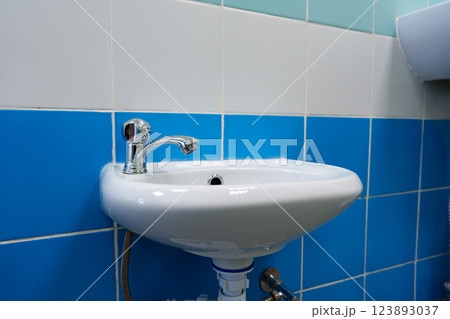 Small white sink with chrome faucet in a tiled bathroom setting during daylight hours Small white sink with chrome faucet in a tiled bathroom setting during daylight hours 123893037