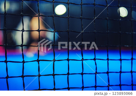 Focus on net at a sports facility with blurred players training during evening hours Focus on net at a sports facility with blurred players training during evening hours 123893066