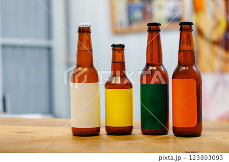 Four bottles of beer with different colored labels sit on a wooden table 123893093