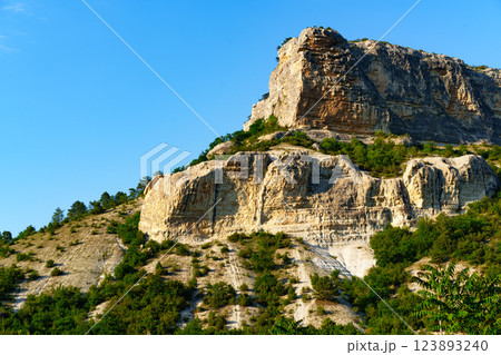 Impressive rocky mountain with lush greenery under a clear blue sky during daylight hours Impressive rocky mountain with lush greenery under a clear blue sky during daylight hours 123893240