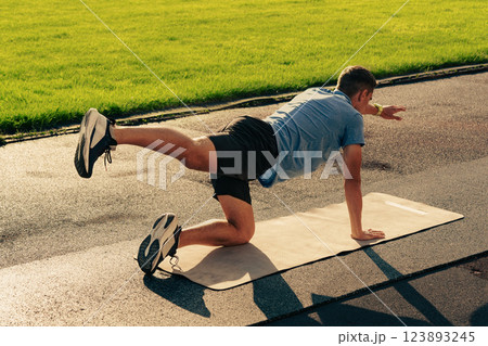 Active individual performing an exercise routine on a mat in a park during daylight Active individual performing an exercise routine on a mat in a park during daylight 123893245