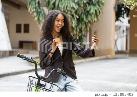 Eco-Consciousness and Connectivity. A woman taking a selfie with her reusable coffee cup while by her bike. Eco-Consciousness and Connectivity. A woman taking a selfie with her reusable coffee cup while by her bike. 123893402