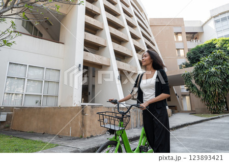 Cycling and Sustainable Living. A young woman stands by her green bicycle outside a modern building, promoting eco-friendly transportation. 123893421