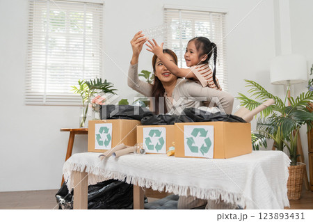 Eco-awareness and Playfulness. A joyful mother-child duo sorting recyclable materials at home. Eco-awareness and Playfulness. A joyful mother-child duo sorting recyclable materials at home. 123893431