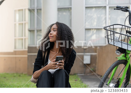 Sustainability and Urban Lifestyle. A young woman reflects while seated next to her green bicycle, embracing eco-friendly transportation. Sustainability and Urban Lifestyle. A young woman reflects while seated next to her green bicycle, embracing eco-friendly transportation. 123893433
