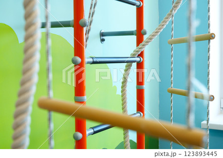 Indoor play area features colorful climbing frame with ropes and wooden bars for children's physical activity and fun 123893445