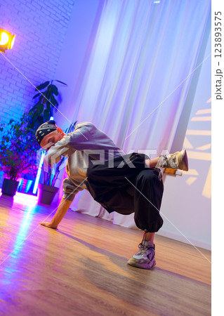 A dancer performs a breakdancing move in a studio with colorful lighting 123893575