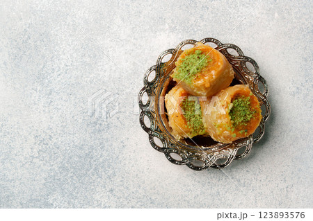 Delicious baklava garnished with pistachios served in an ornate dish on a textured background 123893576