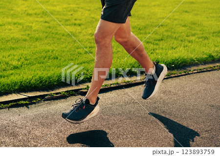 Runner in athletic shoes enjoying a morning jog on a sunny day along a grassy pathway Runner in athletic shoes enjoying a morning jog on a sunny day along a grassy pathway 123893759