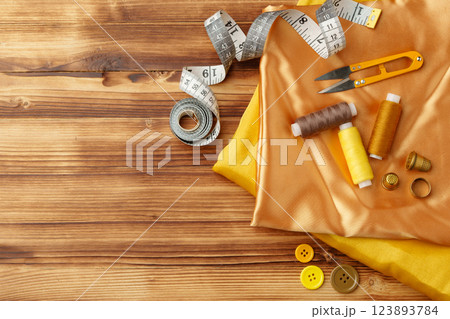 Crafting essentials arranged on golden satin fabric with sewing tools and colorful buttons scattered around 123893784