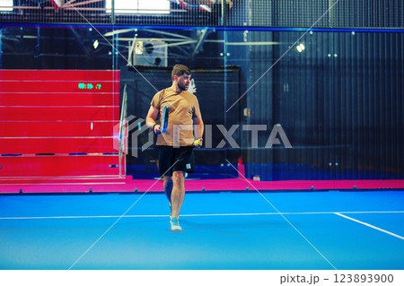 Man practicing badminton in a modern indoor sports facility with vibrant blue flooring and red seating Man practicing badminton in a modern indoor sports facility with vibrant blue flooring and red seating 123893900