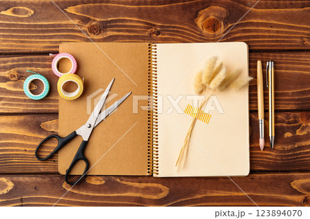 Crafting session with notebook, scissors, and decorative tape on a wooden table Crafting session with notebook, scissors, and decorative tape on a wooden table 123894070