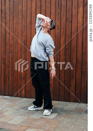 A person in a grey sweatshirt and black pants is striking a pose in front of a wooden wall 123894199