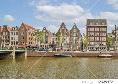 Picturesque scene featuring traditional Dutch buildings along a canal under a clear blue sky, showcasing the charm of Amsterdam's waterfront. 123894721