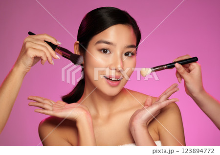 Makeup application on model with playful pose in bright pink background during studio session 123894772